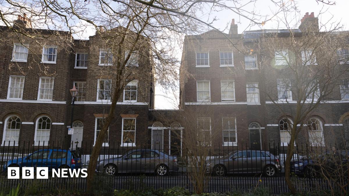 A row of terraced houses, all of which are three storeys high apart from number 25 and 26 which stand at one storey with their front doors next to each other.
