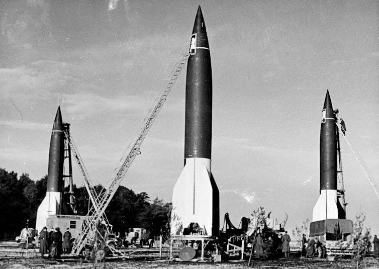 A black-and-white photo of three rockets sitting on a field.