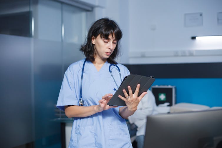 female health professional wearing scrubs in a medical setting and holding a tablet computer.