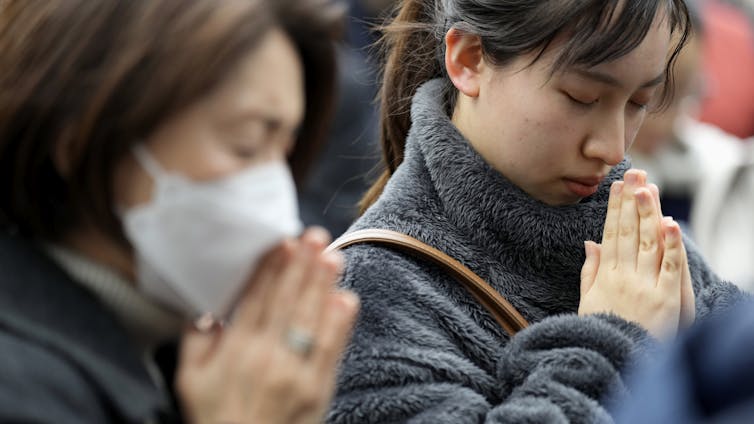 east asian women stand with their hands pressed together and bowing their heads in prayer