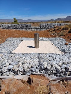 A borehole in a dry brown stream bed with a filter box with gabion in the background.