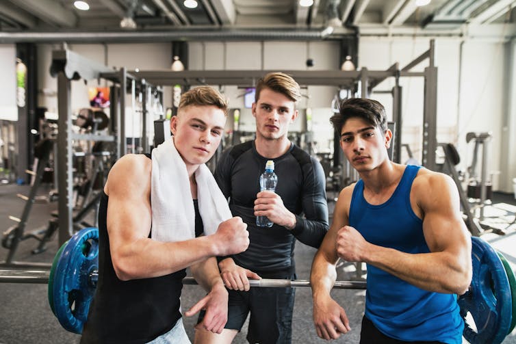 Thee young men displaying their muscles at a gym.