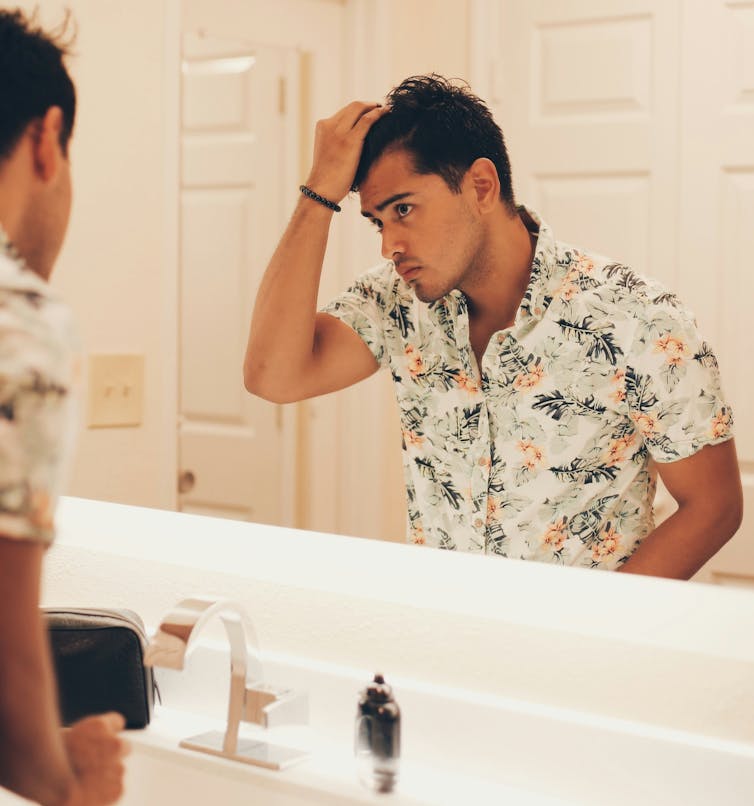 A young man inspecting his looks in front of a mirror.