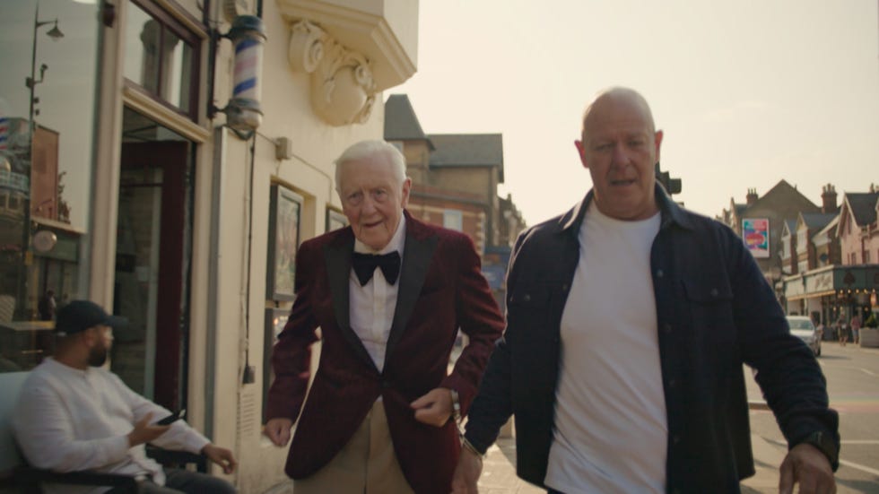George and Benjamin two individuals walking on a street one in formal attire and the other in casual clothing