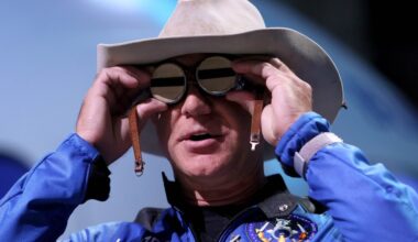 Jeff Bezos holding aviation glasses up to his face.