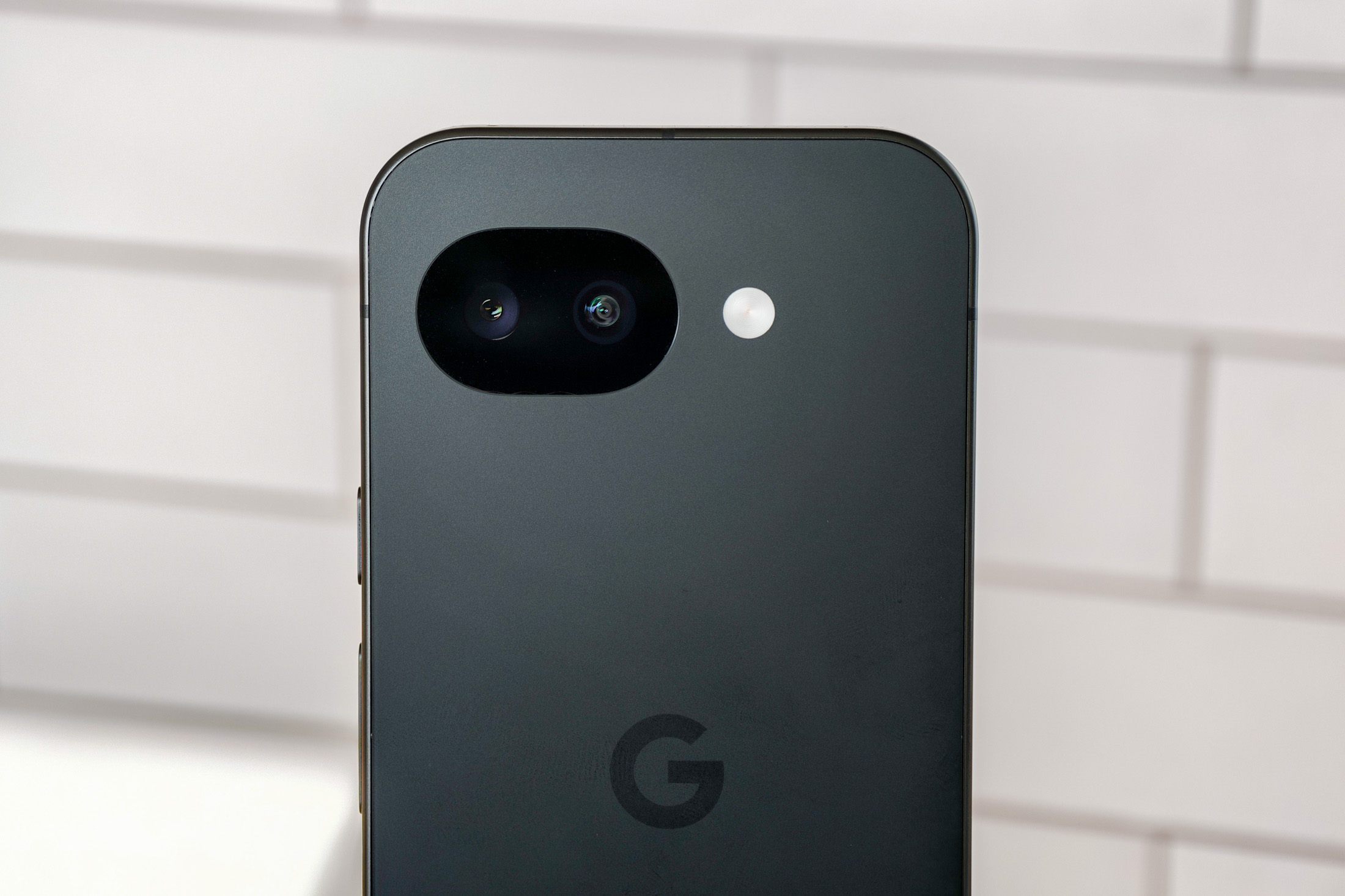 Photo of Google Pixel 10A in front of white tiles, showing the camera head-on