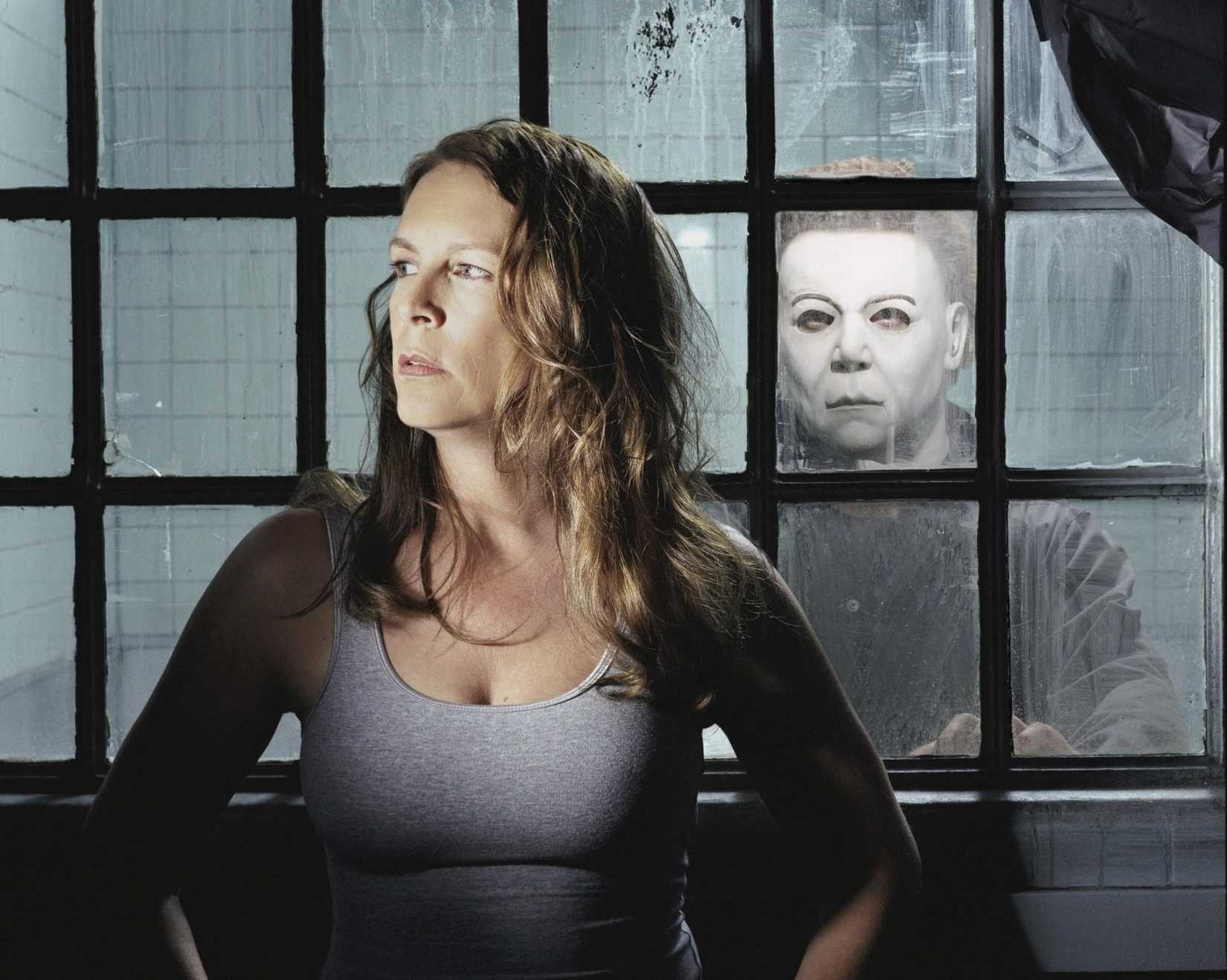 Laurie Strode (Jamie Lee Curtis) stands in front of a series of windows, with the masked Michael Myers waiting on the other side, in a scene from Halloween: Resurrection (2002).