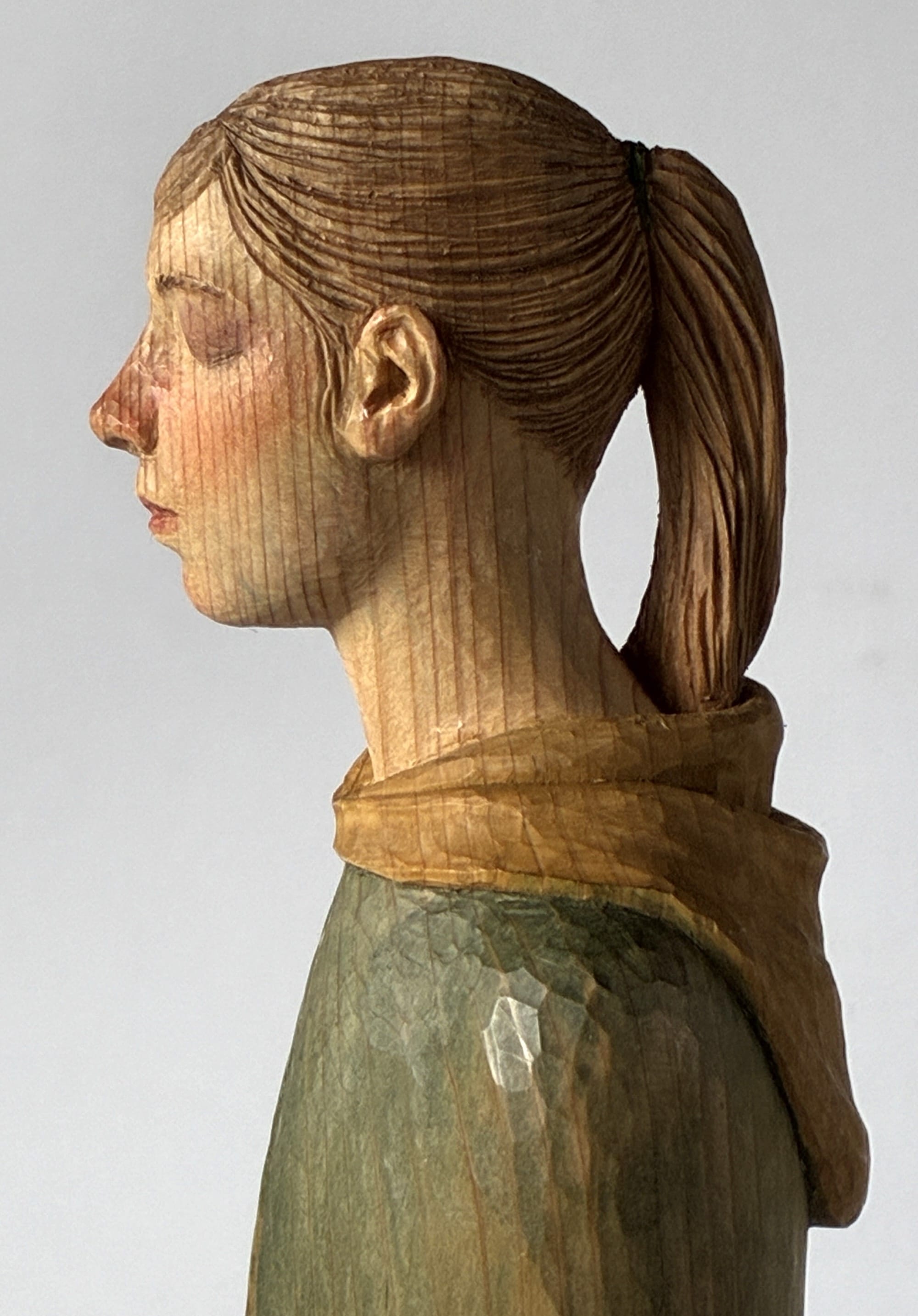 A figurative, painted wood sculpture of a woman with a ponytail by Shinsuke Inoue in profile