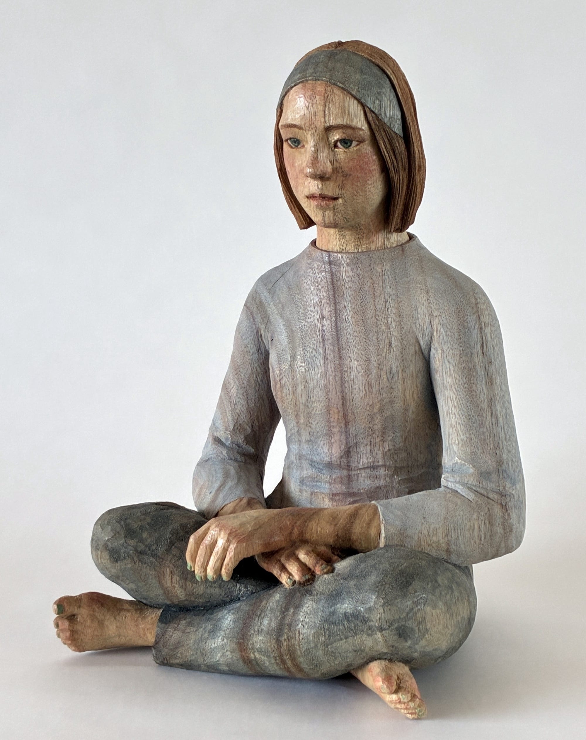 A figurative, painted wood sculpture of a seated young woman in three-quarter profile by Shinsuke Inoue