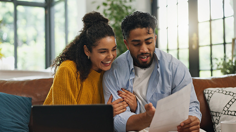 Happy couple looking at paper and laptop in living room