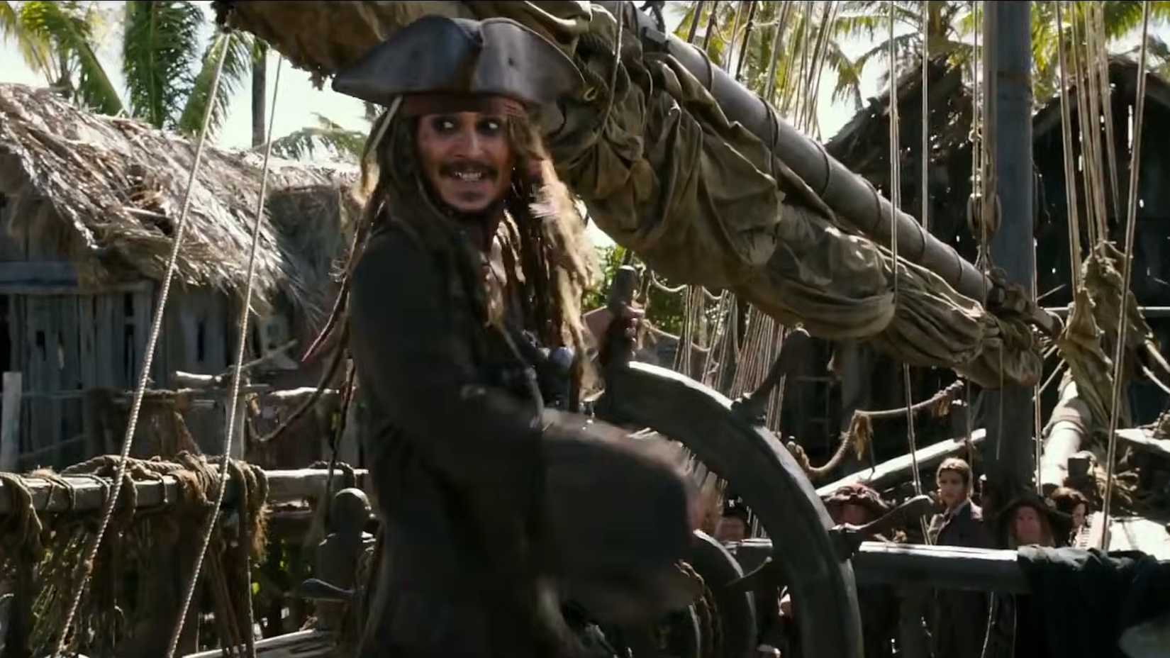 Jack Sparrow grinning behind the wheel of a ship in Pirates of the Caribbean Dead Men Tell No Tales