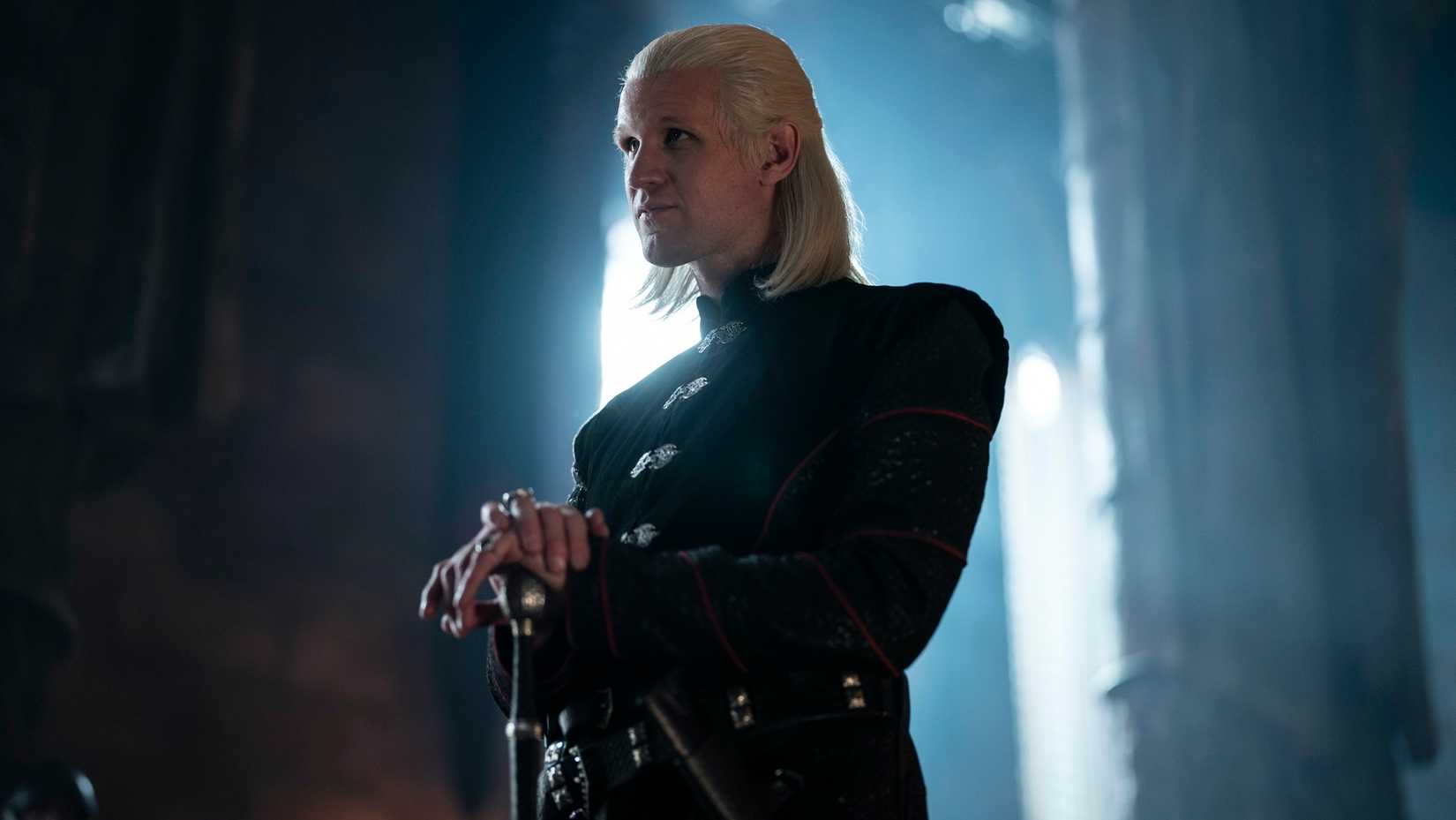 Daemon Targaryen (Matt Smith), a slim blonde man in black, hands resting on the pommel of a sword, in House of the Dragon