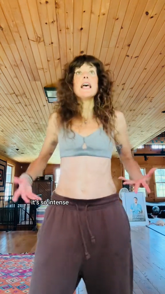 A woman with curly brown hair demonstrates somatic shaking in a room with wood paneling.