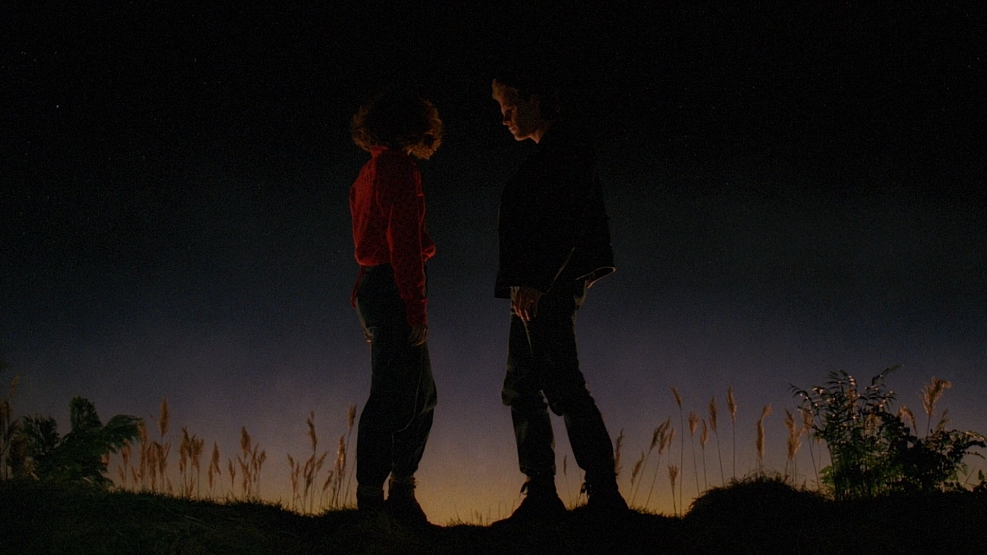A man and a woman stand on a hill, silhouetted by the dawn.