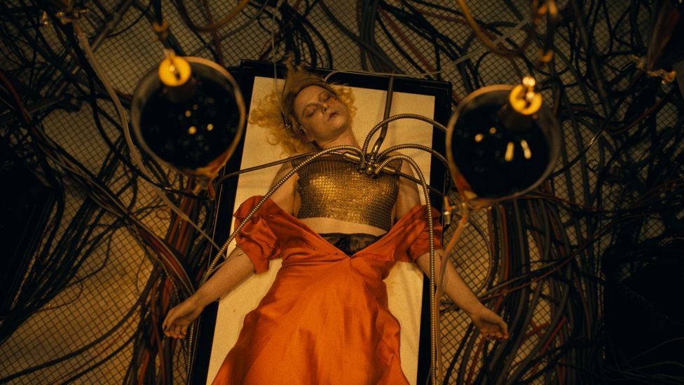 Jessie Buckley as The Bride with blonde hair, lying on table in red dress, with wires attached to her chest (Credit: Warner Bros) Jessie Buckley as The Bride with blonde hair, lying on table in red dress, with wires attached to her chest (Credit: Warner Bros)