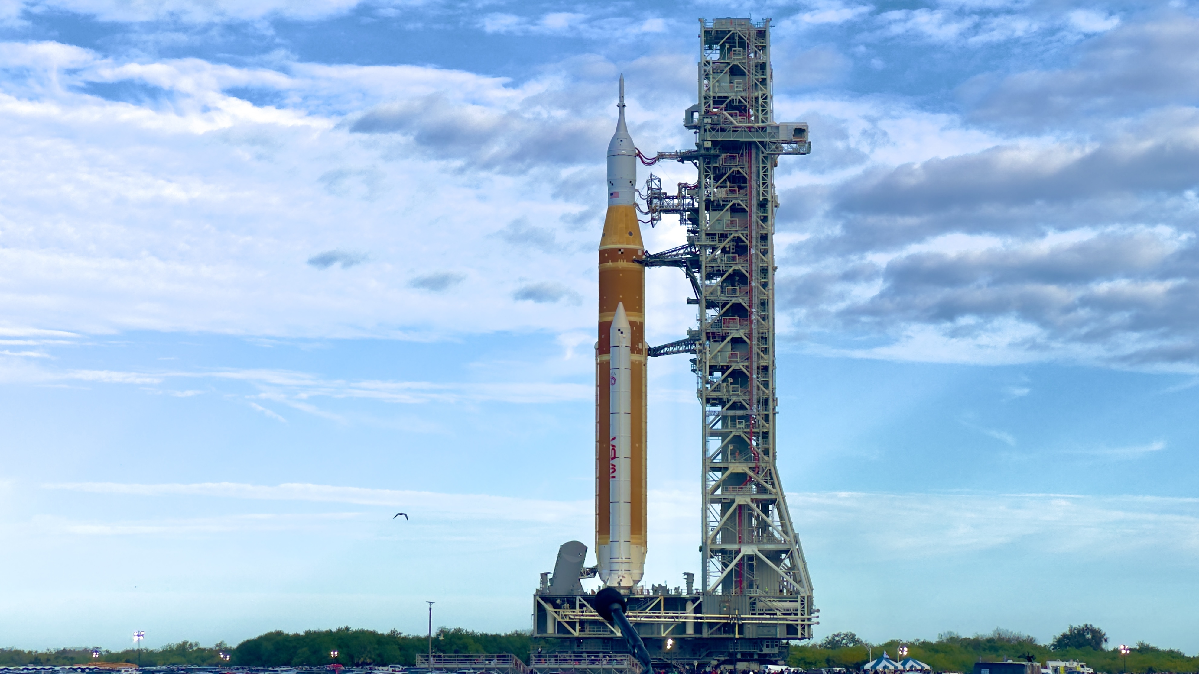 A tall orange rocket stands on a grey platform and tower.