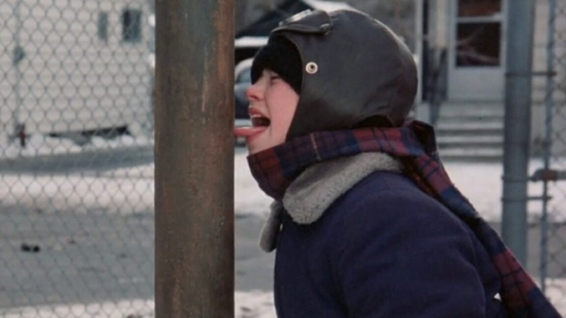 young boy in winter gear, hat and scarf with his tongue sticking out and frozen to a metal pole