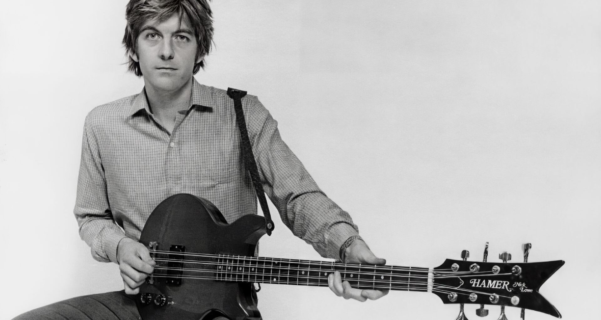 Portrait of musician Nick Lowe playing a Hamer guitar, circa 1990.