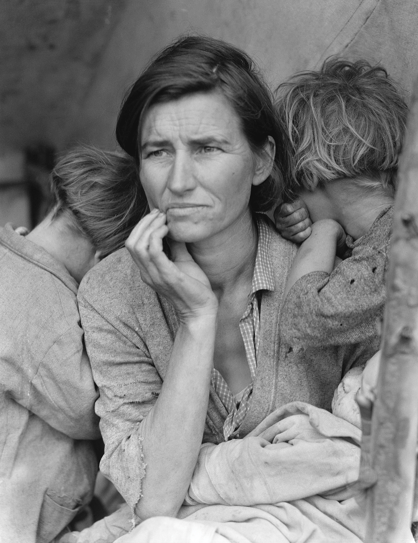 A worried woman with furrowed brows gazes into the distance, cradling her face. Two children lean on her. A black. andwhite photo