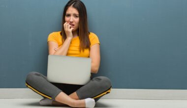 Young woman sitting on the floor with a Windows laptop biting nails, nervous and very anxious