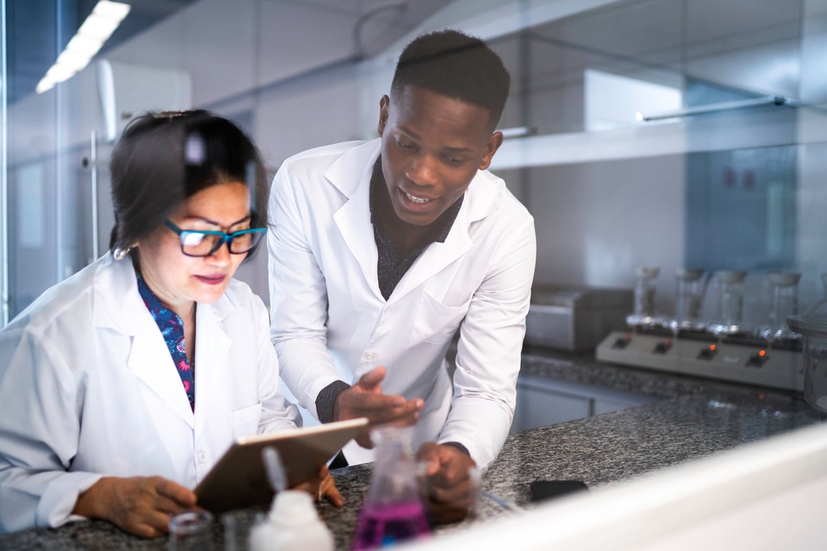 Researchers in white coats discuss trial results in a lab.