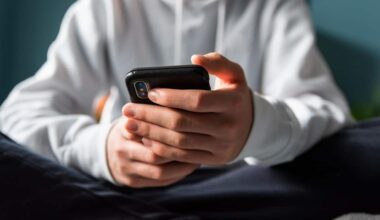 A boy wearing a white sweater, holding a black phone in his hands.