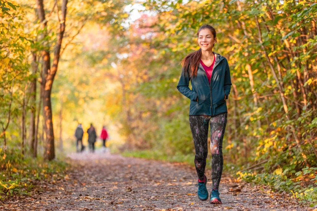 Woman walking on a path through an autumn forest, smiling.
