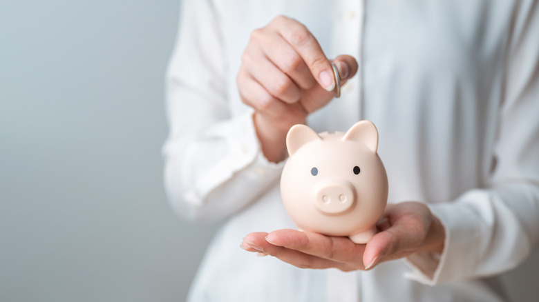 Close-up of a person putting a coin into a piggy bank.