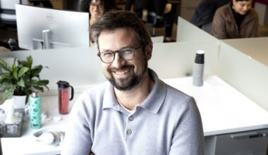 Jonathan Guillemette smiles while standing in an office in front of other employees doing work.