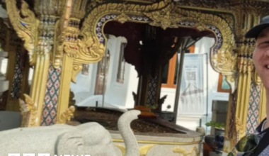 Rory McColl , who is wearing a black baseball cap, takes a selfie in front of a stone elephant and a historic building