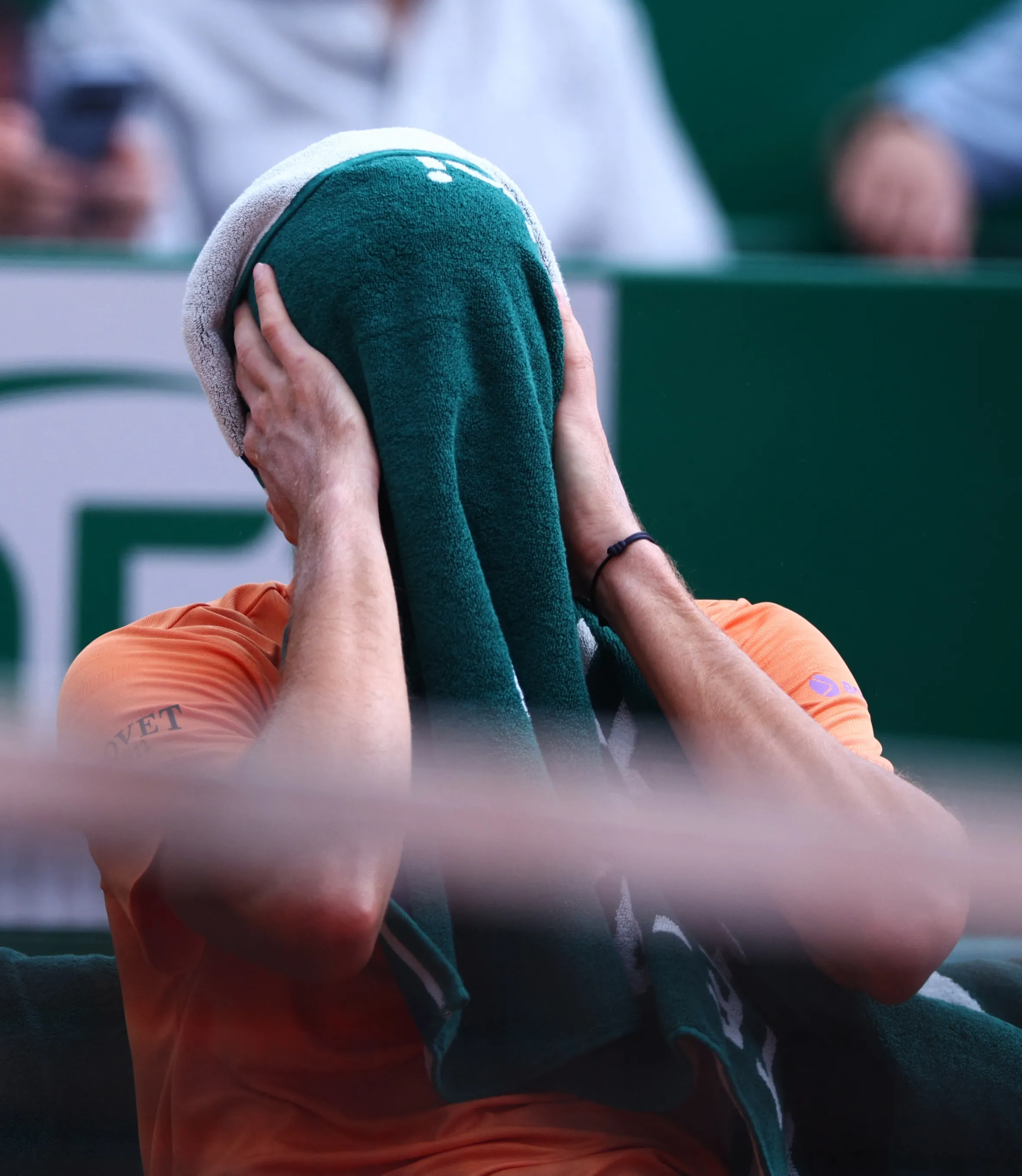 Tennis player Daniil Medvedev covers his head with a green towel during a match.