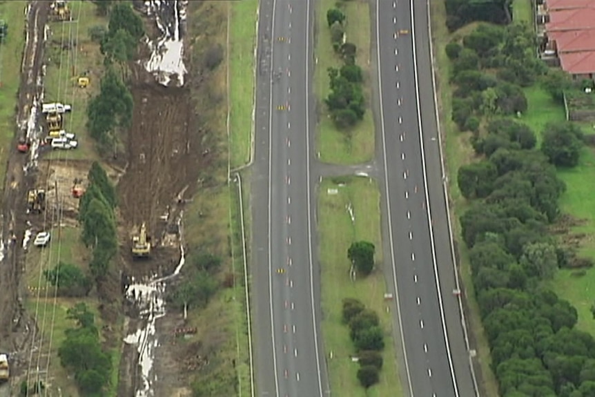 Excavators and emergency workers work on a sinkhole that's adjacent to a freeway