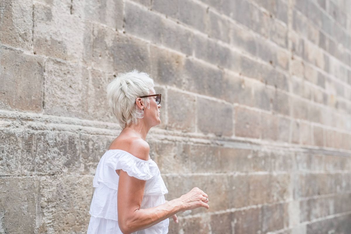 A woman in a white dress is walking down a brick wall. She is wearing glasses and has a serious expression on her face