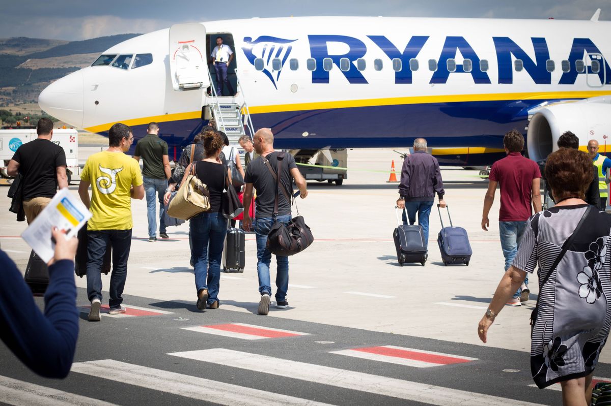 Passengers on the tarmac at Comiso Airport in Sicily walking with carry-on luggage toward a Ryanair airplane