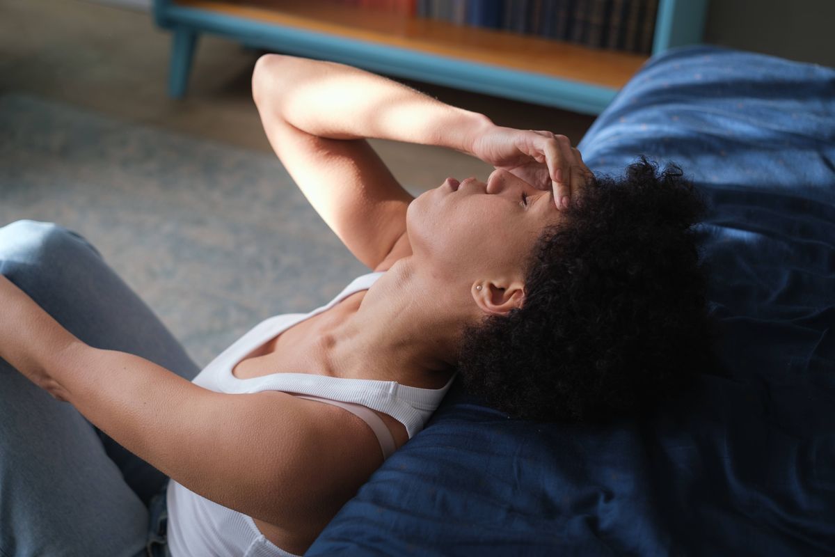 Depressed anxious young African American woman touching forehead, suffering from headache or migraine. Mental burnout. `Sad frustrated female with eyes closed lying on bed