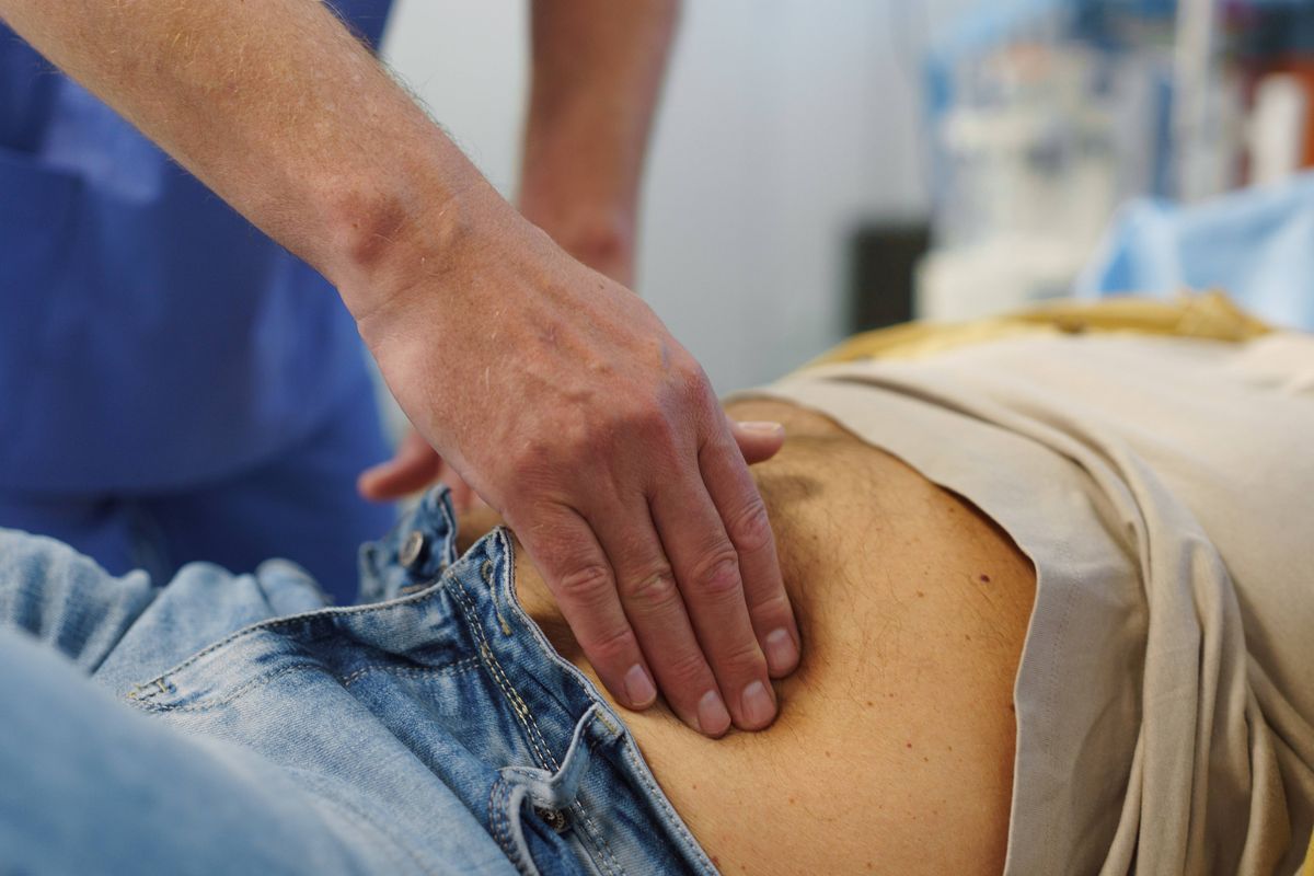 Doctor performing abdominal palpation on senior patient in emergency room.