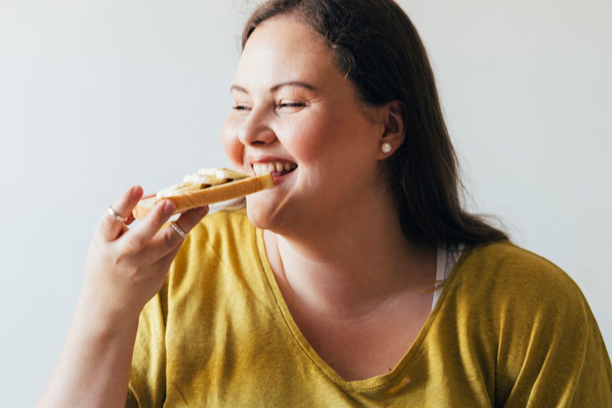 Young Caucasian woman sitting on the bed in her bedroom, eating her breakfast.