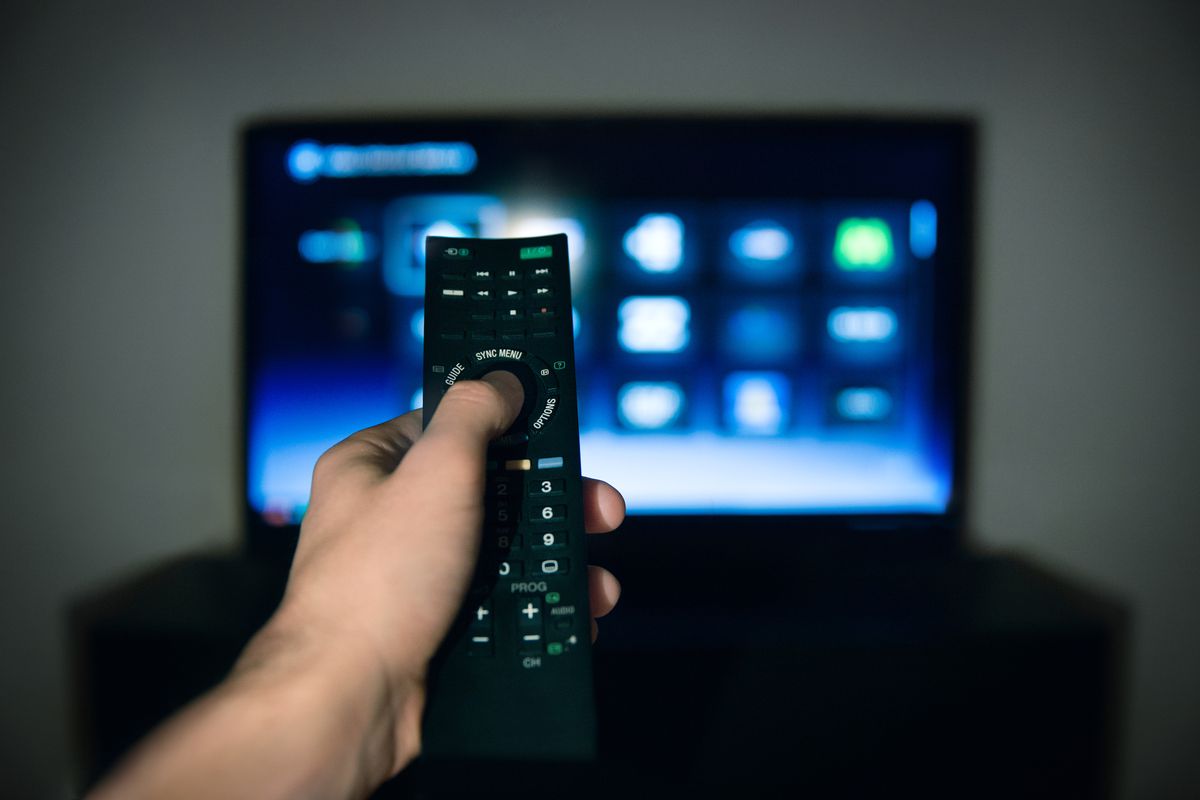 Hand of man pointing remote control at working television screen.