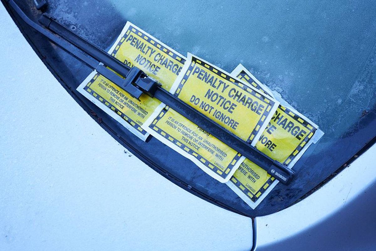 Several yellow parking charge notices affixed to a car's windshield, indicating potential fines for improper parking. The notices are labeled with text and have a distinctive design, placed against the backdrop of the windshield.