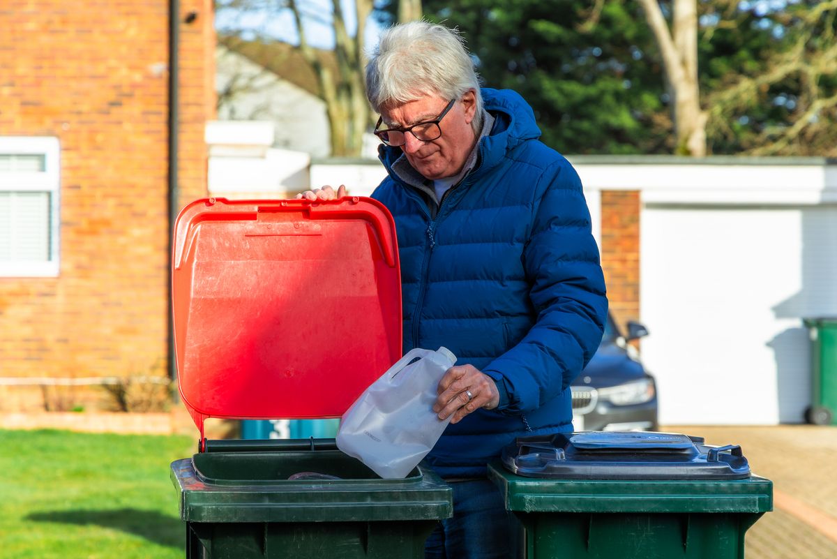 Man in his 70s putting plastic waste into his recycling bin on a residential street