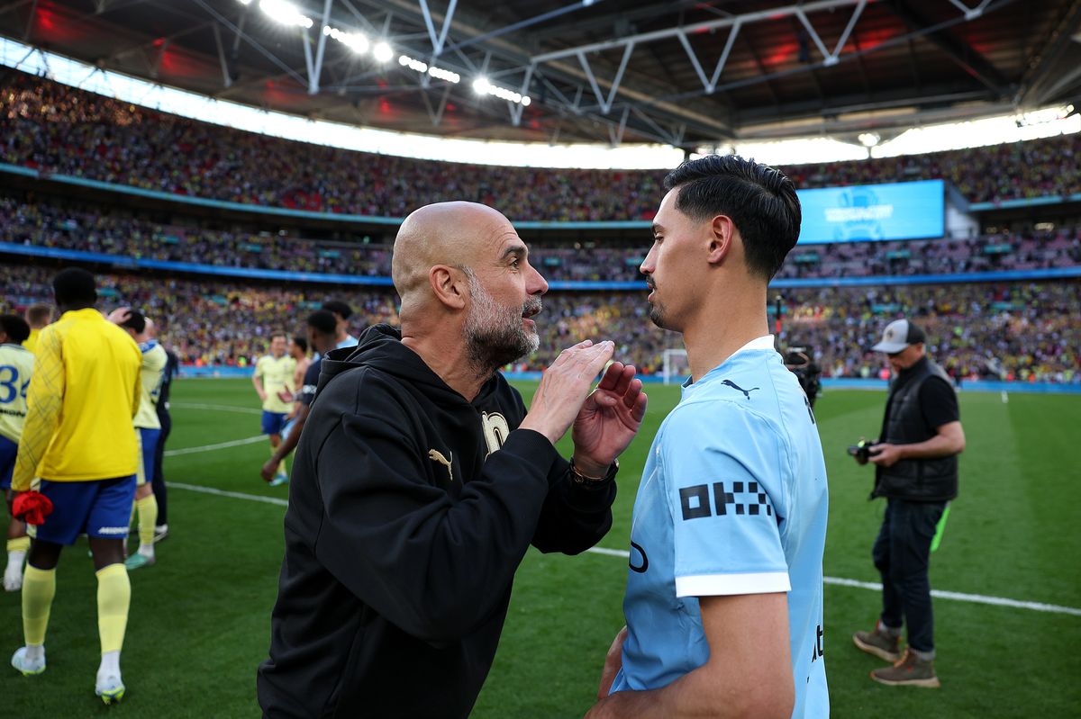 Pep Guardiola, Manager of Manchester City, speaks with Tijjani Reijnders