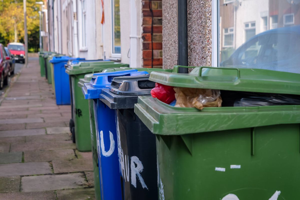 Bins lined up on UK street, with green recycling bin overflowing