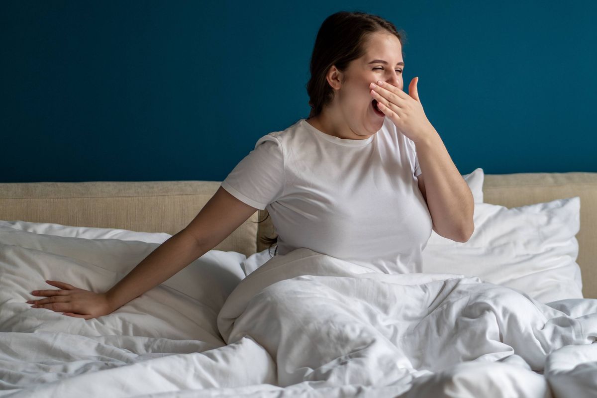 Yawning woman well-rested after good sleep at night, sitting on bed in early morning at home. Drowsy body-positive female in underwear in no hurry to get up, going to spend lazy relaxed weekend
