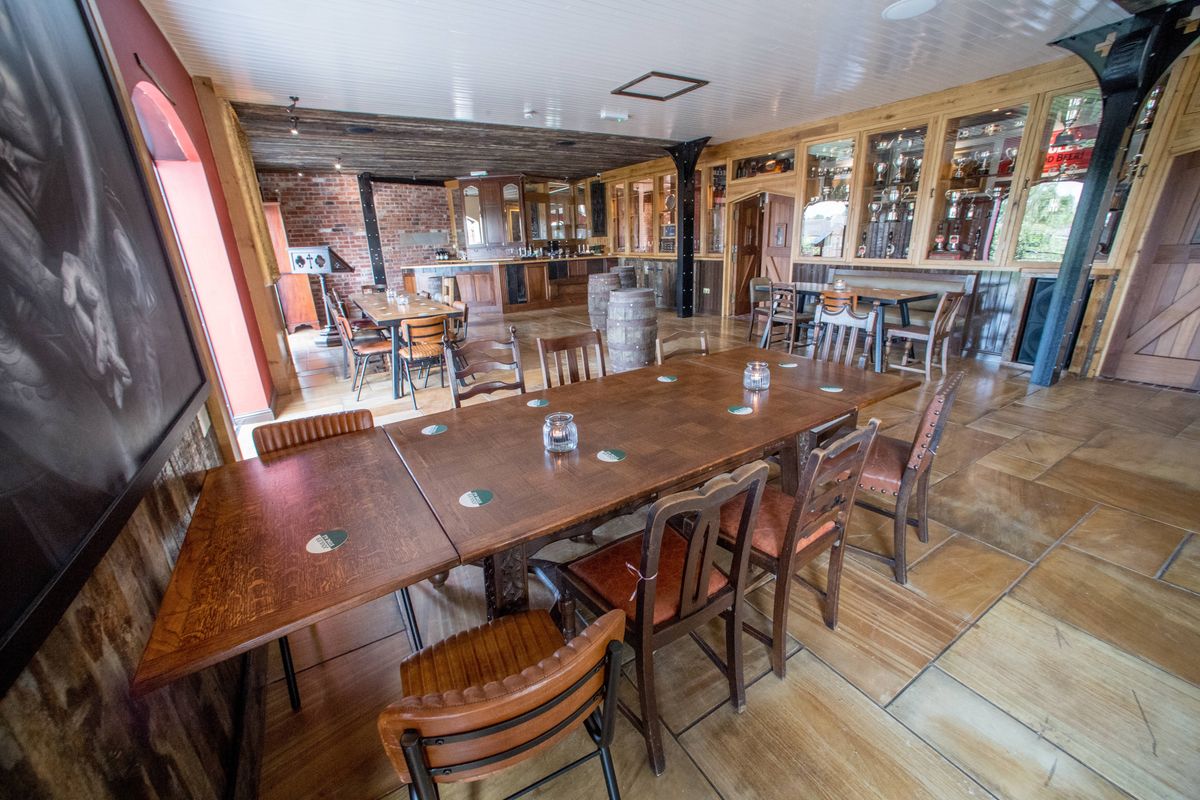An empty interior of a restaurant showcasing a long wooden dining table accompanied by wooden chairs, all set against a backdrop of wooden flooring and red-accented walls.