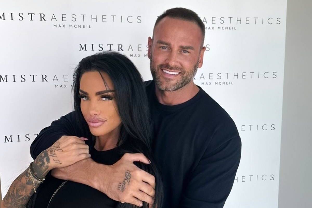 A man and a woman are standing close to each other in front of a banner with text that reads "Mistrasthetics" prominently displayed. The man has a visible smile, and both individuals are dressed in black attire.