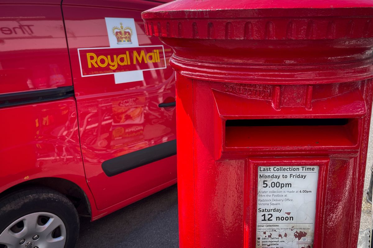 A Royal Mail van waits beside  an original red post box 
