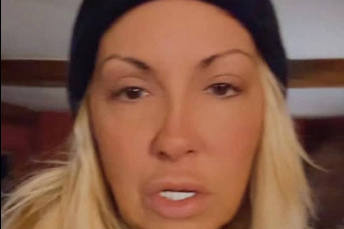 An individual with long, blonde hair, dressed in a black beanie, is captured in a close-up shot. The person is visibly engaged in speaking, with their mouth slightly open, while their eyes are fixed on the camera. The background appears blurred, suggesting a focused foreground on the subject.