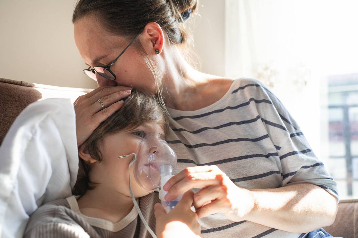An adult female providing respiratory support to another individual using an oxygen mask in a healthcare setting.