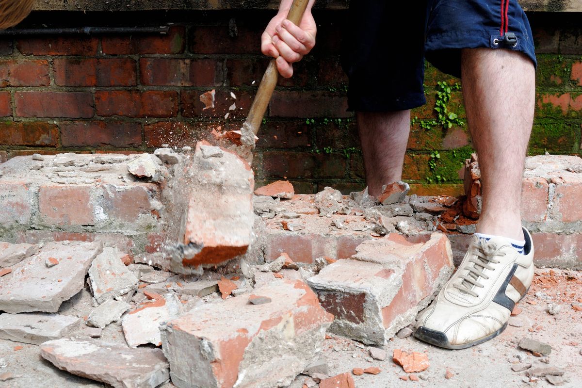 Sledge hammer knocking down brick wall