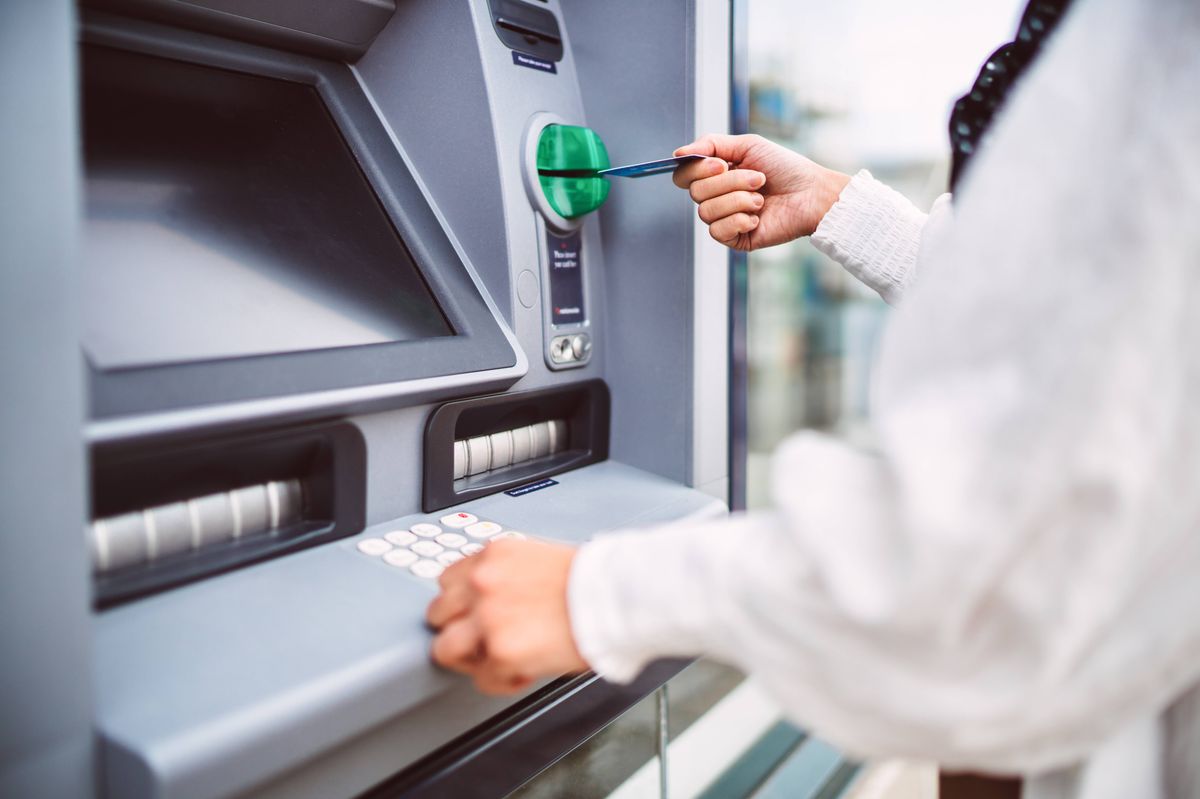 Close-up of hand inserting debit card into automated an ATM machine. Cash withdrawing, paying bills, checking account balance, transferring money, currency exchange at ATM. Self-service concept.
